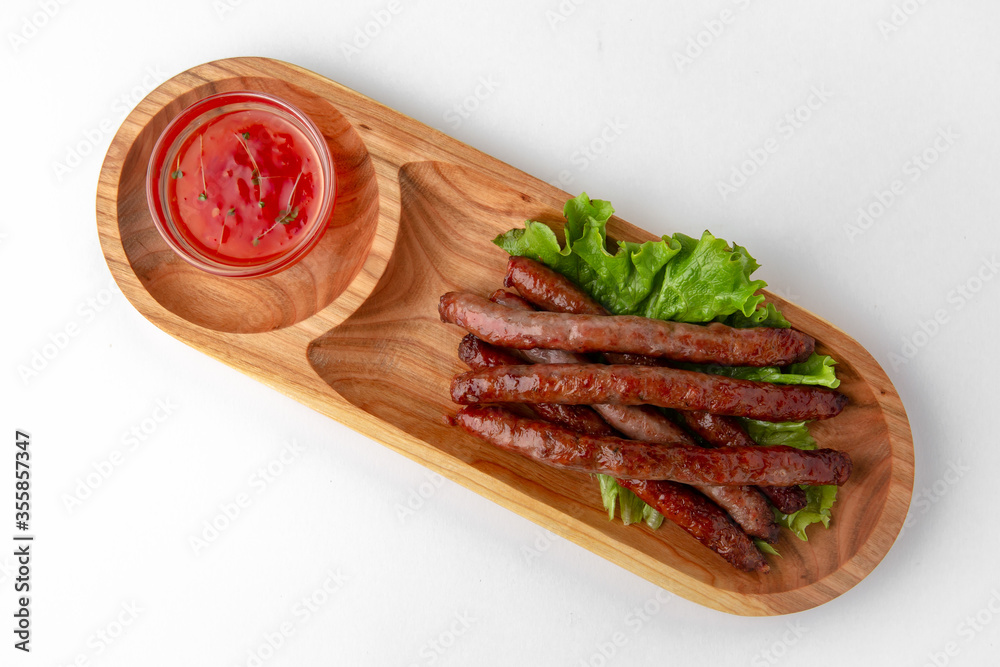 Hunting sausages with sauce on a wooden stand. Banquet festive dishes. Gourmet restaurant menu. White background.