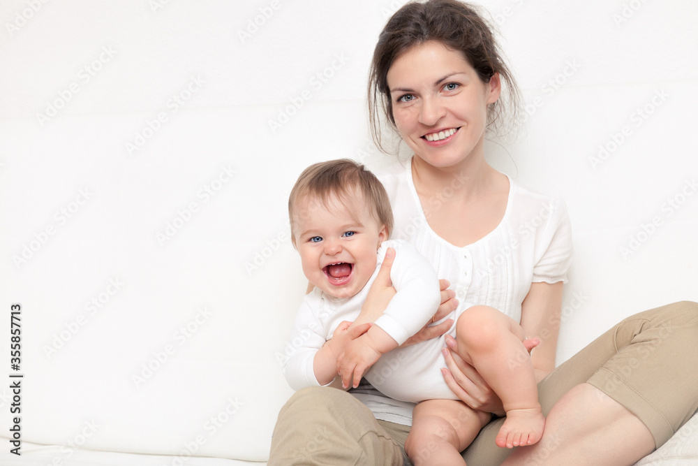 Happy mother playing with baby on white sofa Happy mother playing with baby on white sofa