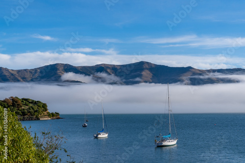 Blue sky, white clouds, mist & aquamarine seas at Akaroa Harbor. Anchored are fishing boats & sailboats, along the Port at Akaroa, Canterbury, New Zealand. © tonklafoto