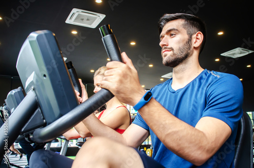 Portrait of young man exercising using stationary bike in gym with a group of people. Fitness class doing sport biking in the gym for health