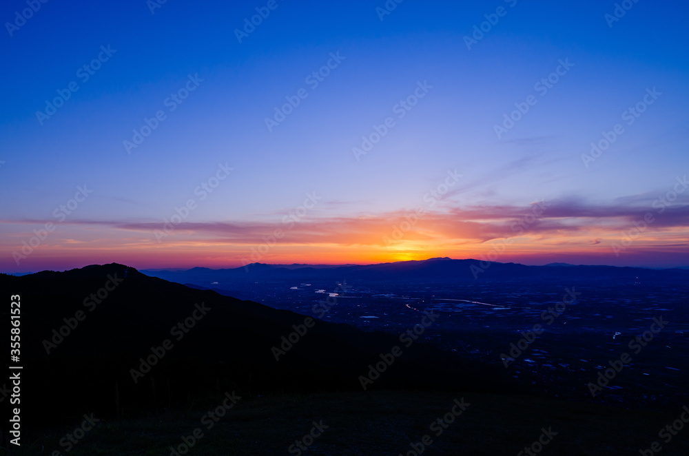 山に沈む夕焼けと河と平野