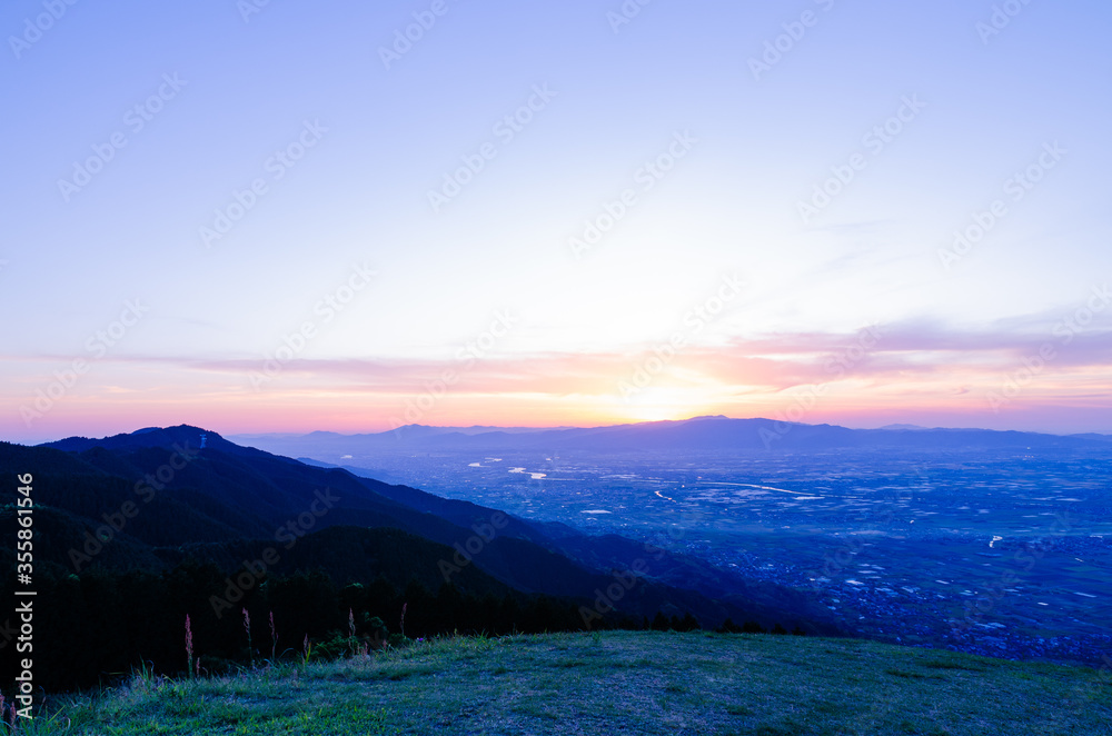 Naklejka premium 山に沈む夕焼けと河と平野