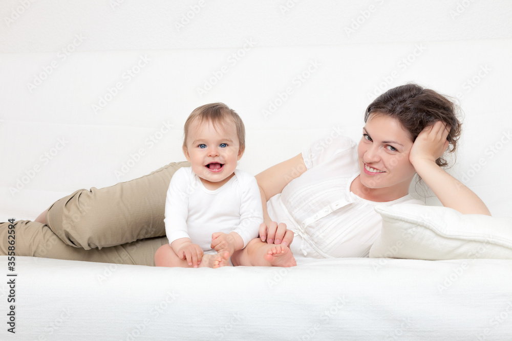 Happy mother playing with baby on white sofa Happy mother playing with baby on white sofa