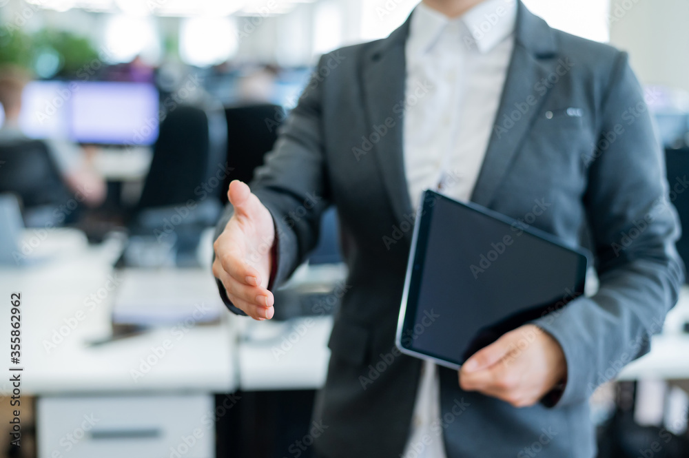 Woman office worker holds out her hand for greeting. Faceless business lady is holding a digital tablet and a handshake in an agreement to a successful transaction. Woman office worker holds out her hand for greeting. Faceless business lady is holding a digital tablet and a handshake in an agreement to a successful transaction.