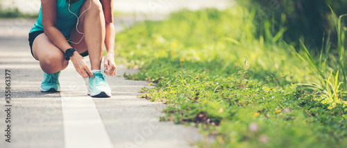 Running woman tying laces of running shoes before jogging through the road in the workout nature park. Weight Loss and Healthy Concept, copy space for banner