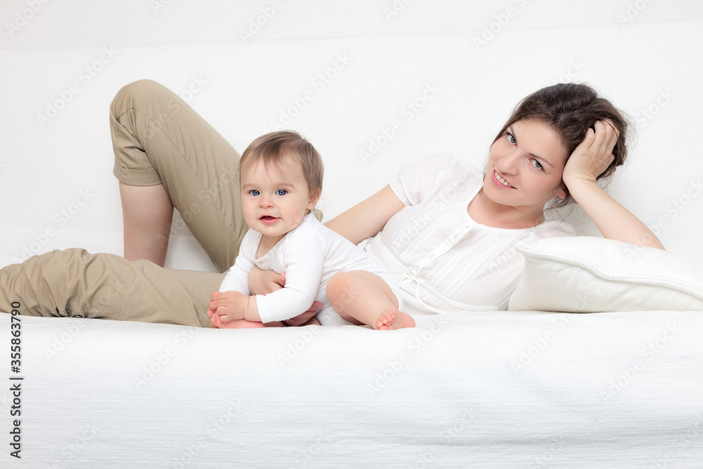 Happy mother playing with baby on white sofa Happy mother playing with baby on white sofa