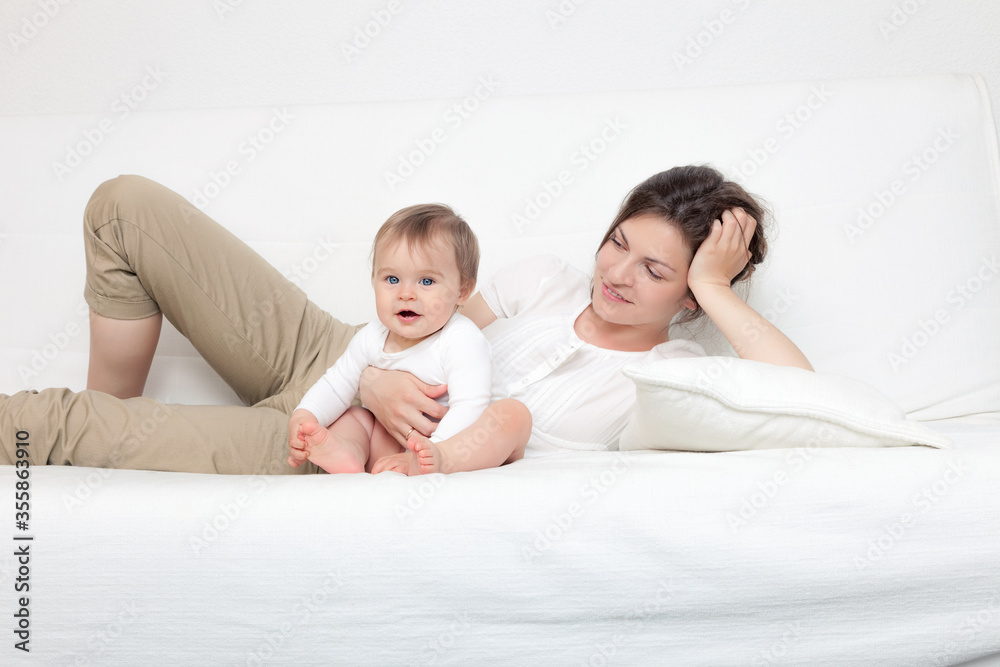 Happy mother playing with baby on white sofa Happy mother playing with baby on white sofa