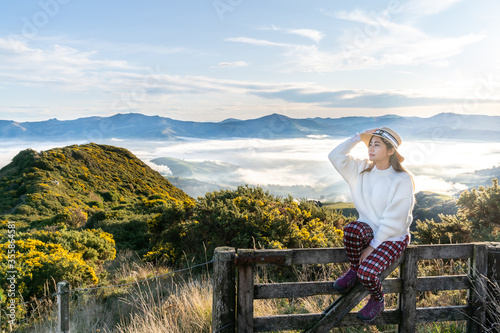 Happy carefree asian woman enjoying nature with layers of mountains and the mist in the morning at The peak of Bank Peninsula  Akaroa  New Zealand.