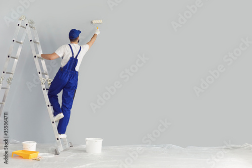 Building contractor painting grey wall with roller brush, copy space text. Construction worker renovating house photo