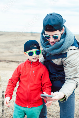 young father with his son having fun outside in spring field, happy family smiling, lifestyle people making selfie wearing sunglasses