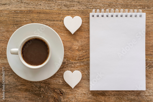 Coffee cup and blank notebook paper on wooden table. Coffee break concept.