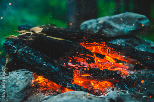 Vivid smoldered firewoods burned in fire closeup. Atmospheric background with orange flame of campfire. Full frame image of bonfire with sparks in bokeh. Warm vortex of glowing embers and ashes in air