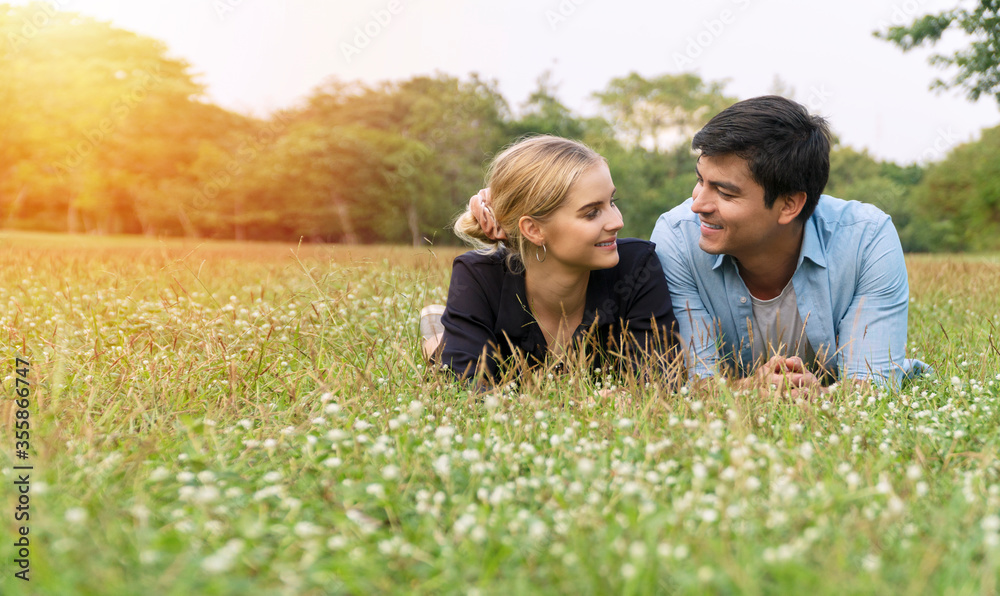 Joyful young couple looking each other lying together on the green grass in summer sunny park feeling relaxation. Lifestyle and relationship concept. Joyful young couple looking each other lying together on the green grass in summer sunny park feeling relaxation. Lifestyle and relationship concept.
