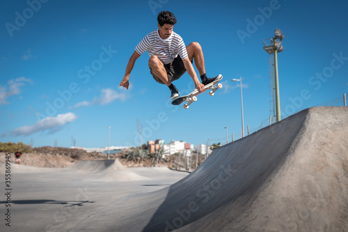 Hombre joven hace un truco llamado "boneless" en rampa con su tabla de skate en un parque.