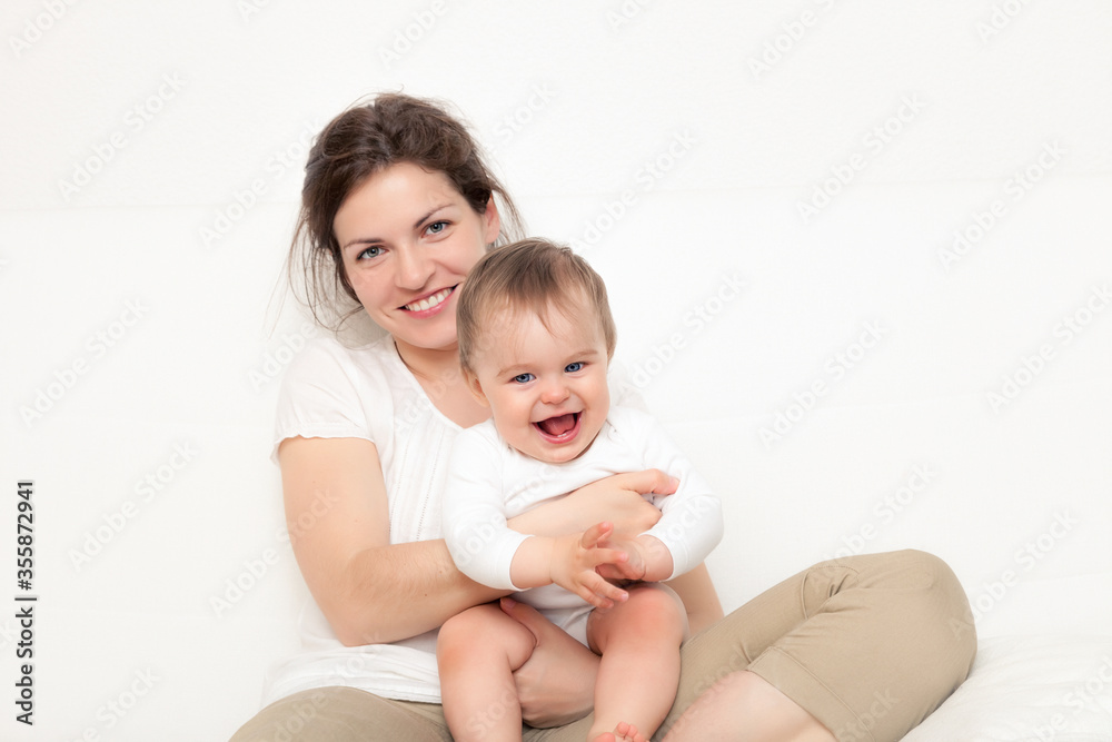 Happy mother playing with baby on white sofa Happy mother playing with baby on white sofa