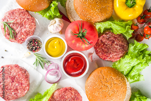 Cooking burger background. Set various cheeseburger and beefburger ingredients - bun, tomatoes, onion, lettuce, sauces, cheese and raw burger cutlets, ready for barbecue grill. Burger bbq party fest 