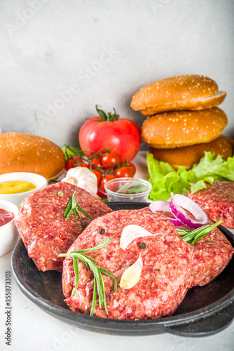 Cooking burger background. Set various cheeseburger and beefburger ingredients - bun, tomatoes, onion, lettuce, sauces, cheese and raw burger cutlets, ready for barbecue grill. Burger bbq party fest 