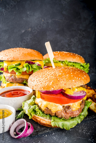 Tasty grilled homemade cheeseburgers with beef, tomato, cheese, tomato and lettuce. On dark grey background, with sauces. Top view copy space