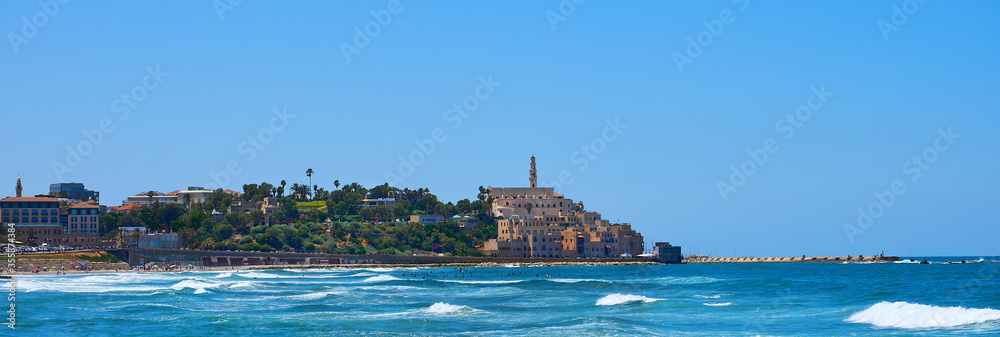 Alma beach in Tel Aviv-Yafo in a beautiful bright summer day people swimming in the blue ocean water near the shore of the old town in Jaffa without any clouds in the blue clear sky 