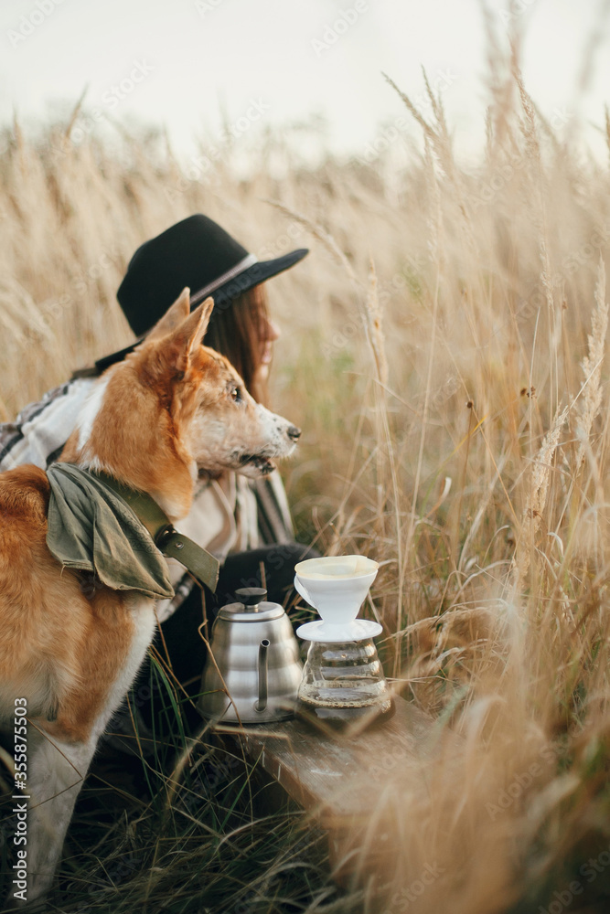 Φωτογραφία Hipster traveler hugging her golden dog, sitting at fresh coffee brewing in filter dropper in rural countryside herbs in sunset