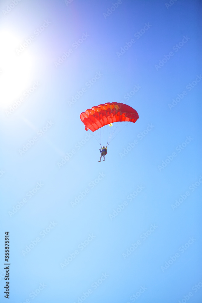 A man parachutes to the ground against a blue Sunny sky. The sun shines on the skydiver, skydiving landing with a parachute. A man parachutes to the ground against a blue Sunny sky. The sun shines on the skydiver, skydiving landing with a parachute.