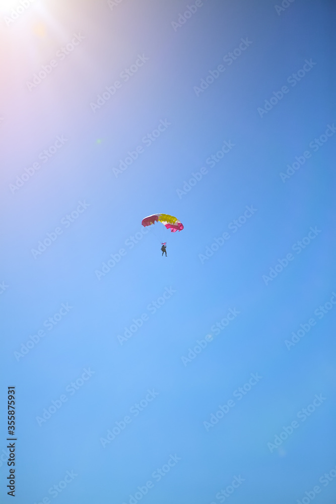 A man parachutes to the ground against a blue Sunny sky. The sun shines on the skydiver, skydiving landing with a parachute. A man parachutes to the ground against a blue Sunny sky. The sun shines on the skydiver, skydiving landing with a parachute.
