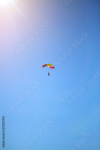 A man parachutes to the ground against a blue Sunny sky. The sun shines on the skydiver, skydiving landing with a parachute.