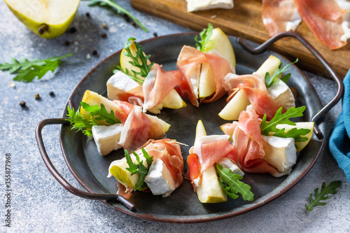 Summer snacks. Pear appetizer with jamon, arugula and brie cheese on a light stone table.