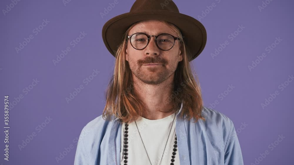 Bearded fellow in casual outfit, glasses, hat. He yawning and covering mouth with palm while posing on purple studio background. Close up Bearded fellow in casual outfit, glasses, hat. He yawning and covering mouth with palm while posing on purple studio background. Close up
