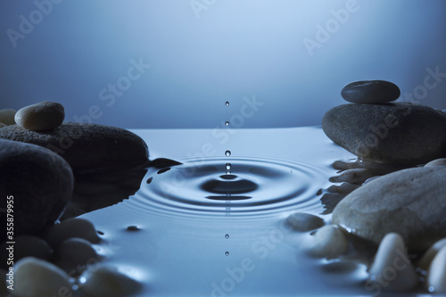 Perfect water drop in a pond with ripples. Blue tones to reflect puddle in night time surrounded by pebbles. Peaceful tranquility.