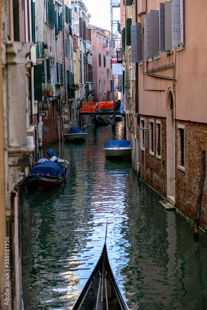 vertical photo of a narrow venetian canal flowing between brick buildings