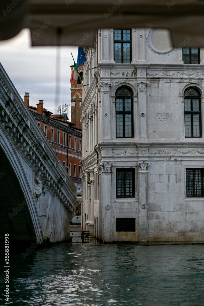horizontal photo of a venetian canal flowing under a beautiful concrete bridge