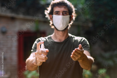 Man with face mask spraying alcohol on his hands outside.