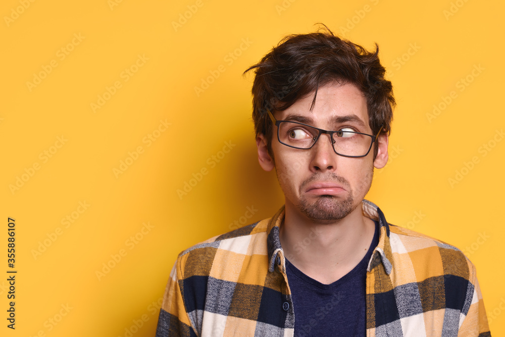 Obraz premium Portrait of sad caucasian man in eyeglasses looking at free copy space for text, information, advertising, isolated on yellow studio wall. Funny guy staring with fear aside. Human emotions concept