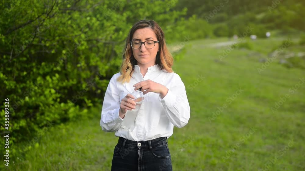 A young adult girl drinks water from a bottle. she is in nature, dressed in a white shirt and black jeans. A young adult girl drinks water from a bottle. she is in nature, dressed in a white shirt and black jeans.