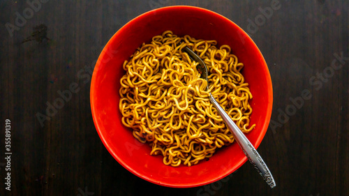 Tableau sur toile Top view of fried instant noodle or maggie with fork in a red bowl with wooden background
