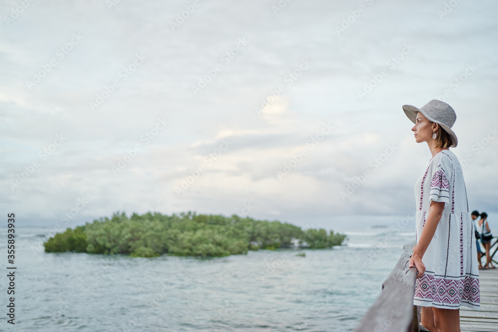 Vacation on tropical island. Woman in hat enjoying sea view from wooden terrace,