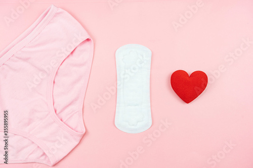 Top view white sanitary napkin red heart and pink underpants isolated on pink background. Woman hygiene  Concept of critical days  menstruation health care