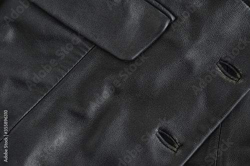 Black genuine worn leather texture with buttonholes and pocket flap. Element of an old vintage jacket. Dark background. Closeup. Focus stacking photo
