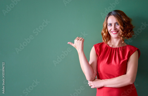 Copy space for avertisement. Portrait of happy smiling young woman pointing away against green wall.