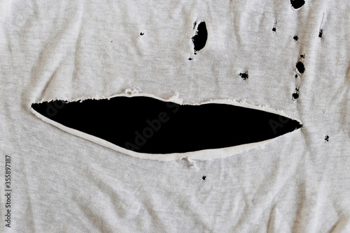 Grunge damaged cloth on black background. Gray white fabric with big hole. Texture of an old dirty ragged t shirt. Copy space