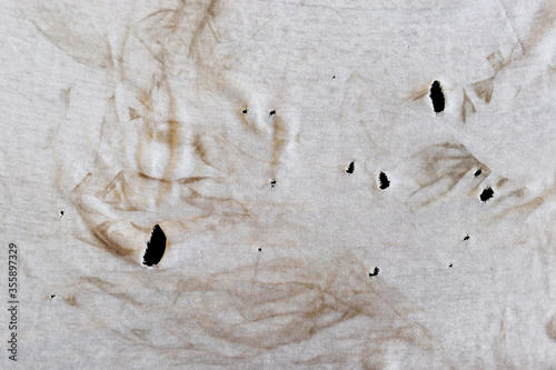 Texture of an old dirty ragged t shirt with brown stains. Dirty white cloth with many holes on black background. Crumpled torn rag. Copy space