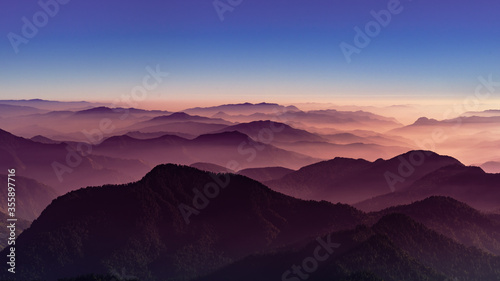 View of Himalayas mountain range with visible silhouettes through the colorful fog from Khalia top trek trail. Khalia top is at an altitude of 3500m himalayan region of Kumaon  Uttarakhand  India.