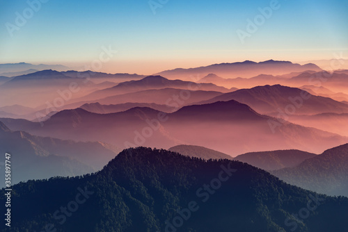 View of Himalayas mountain range with visible silhouettes through the colorful fog from Khalia top trek trail. Khalia top is at an altitude of 3500m himalayan region of Kumaon  Uttarakhand  India.
