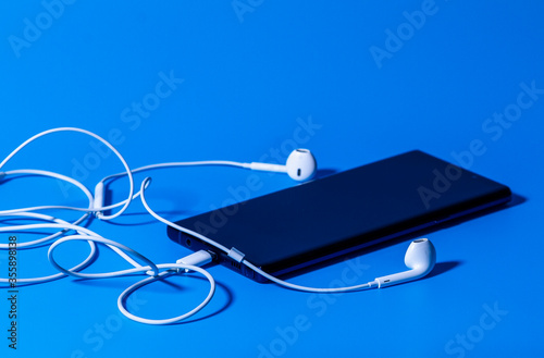 Smartphone with headphones on a blue background. Side view.