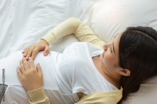 Happy pregnant mother touching beautiful belly laying down in cozy bed at home. prenatal, pregnancy, motherhood, expectation concept Young pregnancy asian girl get happiness, smile face. Mom love baby