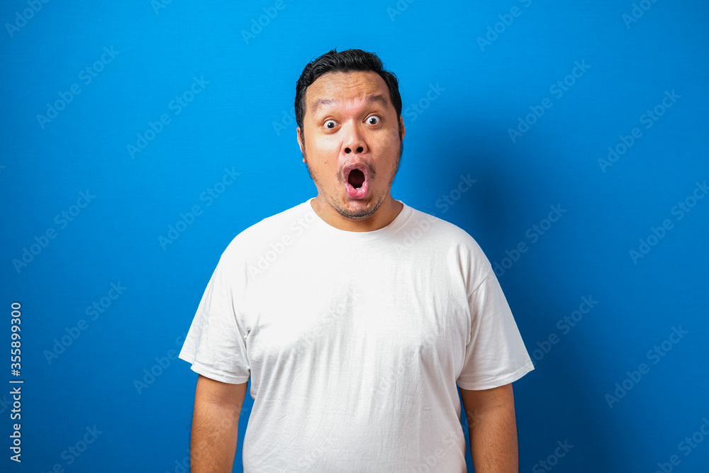 Fat Asian man in white t-shirt shows funny shocked and surprise expression against blue background Fat Asian man in white t-shirt shows funny shocked and surprise expression against blue background