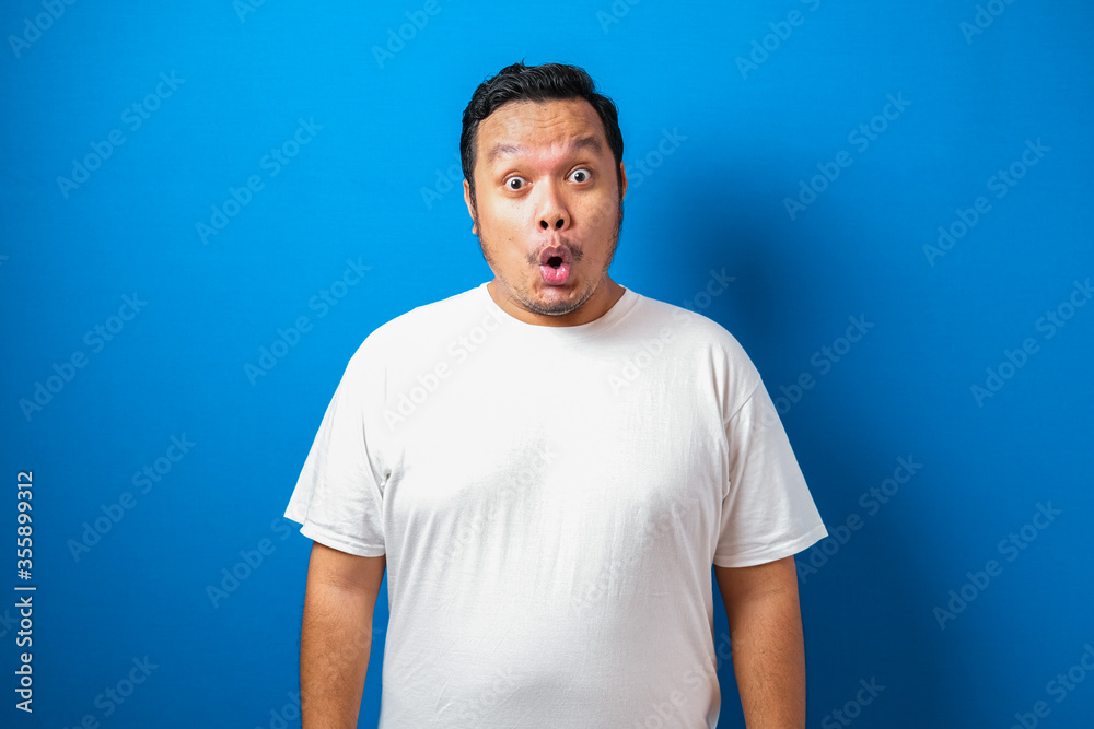 Fat Asian man in white t-shirt shows funny shocked and surprise expression against blue background Fat Asian man in white t-shirt shows funny shocked and surprise expression against blue background