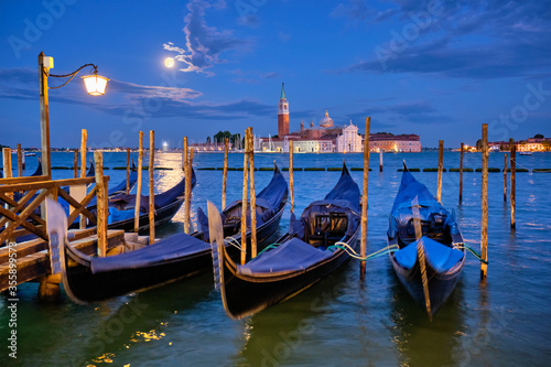 Romantic vacation Venice travel background - gondolas at Saint Mark (San Marco) square and Basilica San Giorgio Maggiore Church seen across Venice lagoon with full moon. Venice, Italy