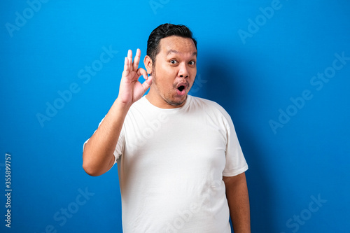 Young Fat Asian man smiling with ok sign. Happy asian man over blue background doing okay sign.